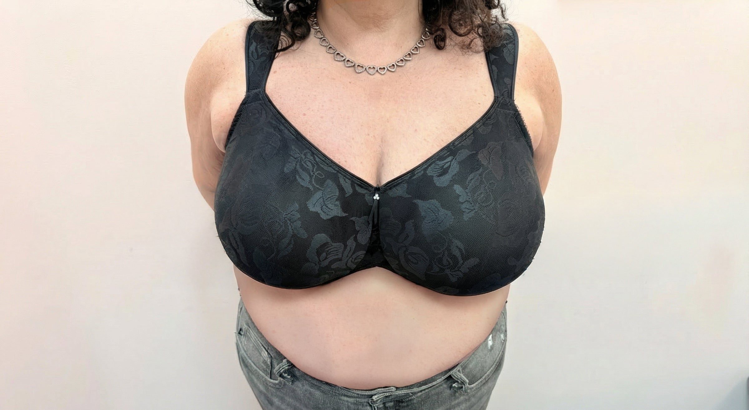 A woman wearing a black floral-patterned underwire bra and gray jeans