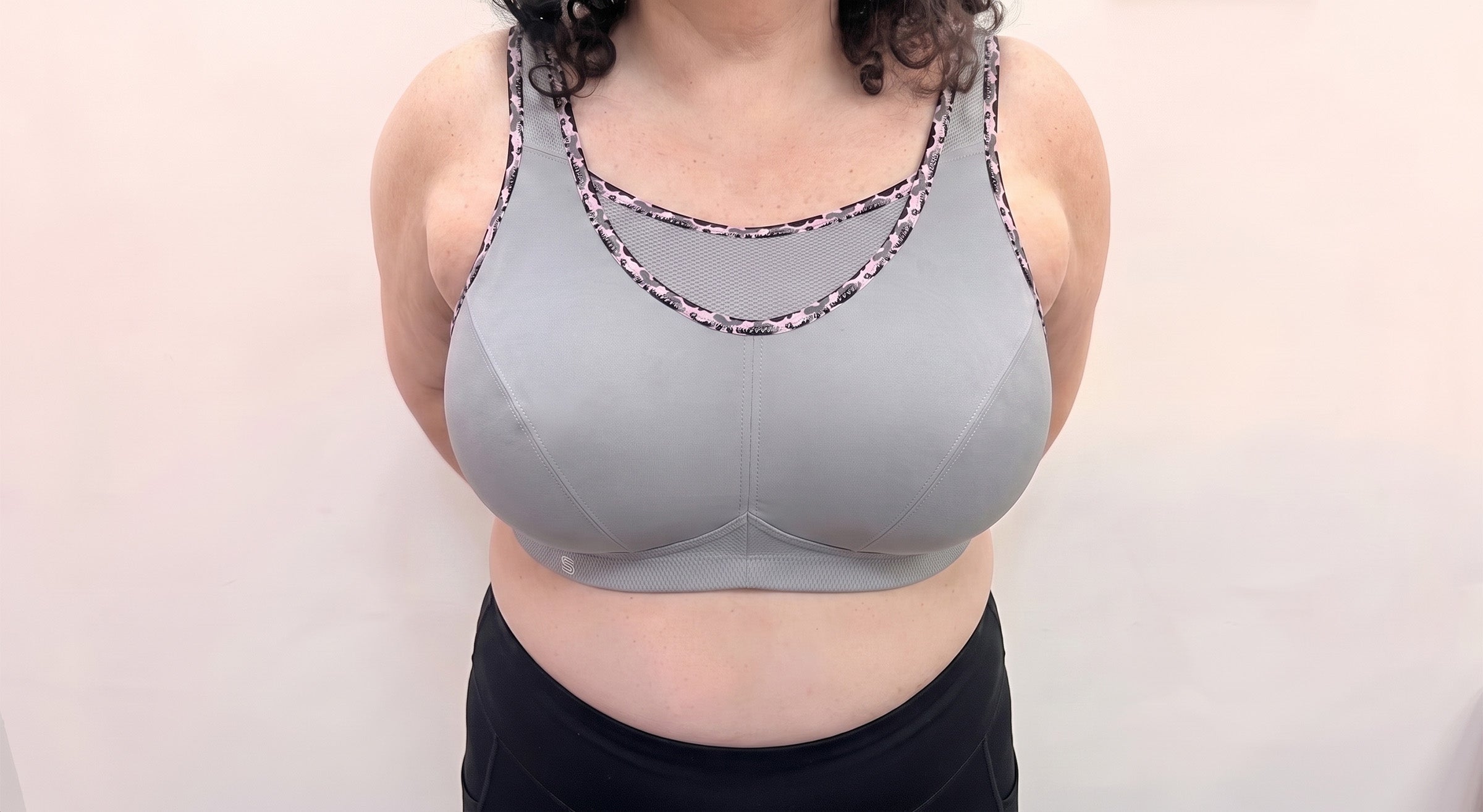 A woman wearing a light gray sports bra with patterned trim and black bottoms, standing against a plain light background.