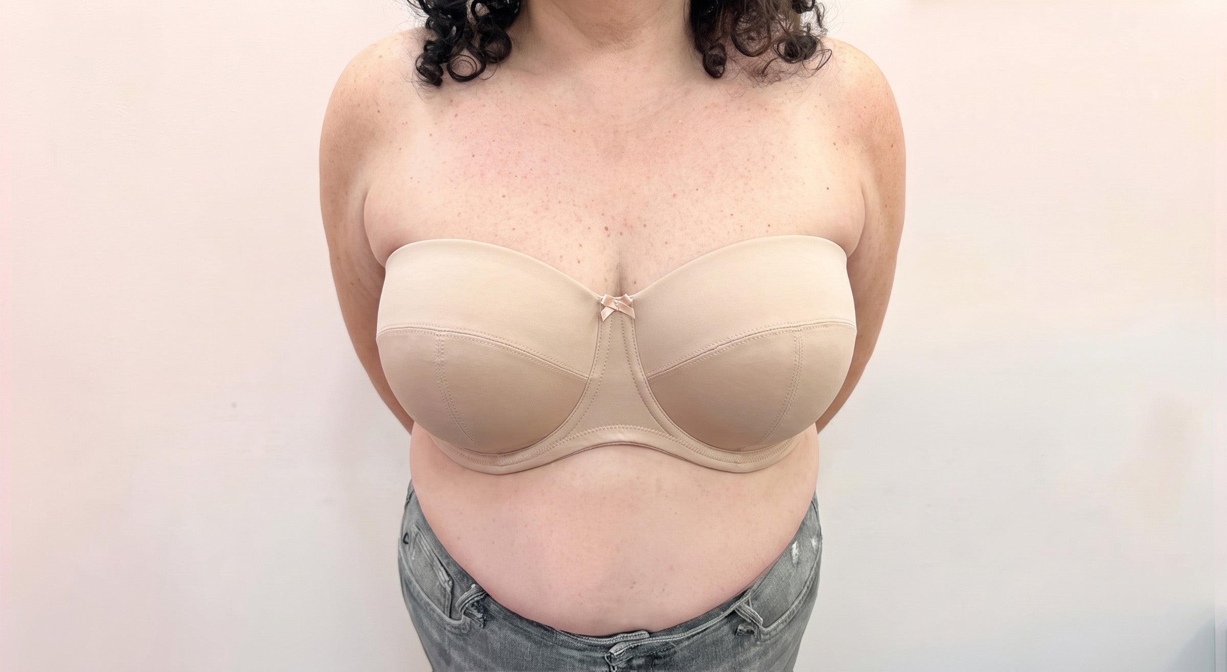 A person wearing a beige strapless underwire bra, shown from the shoulders to the hips against a plain light background.