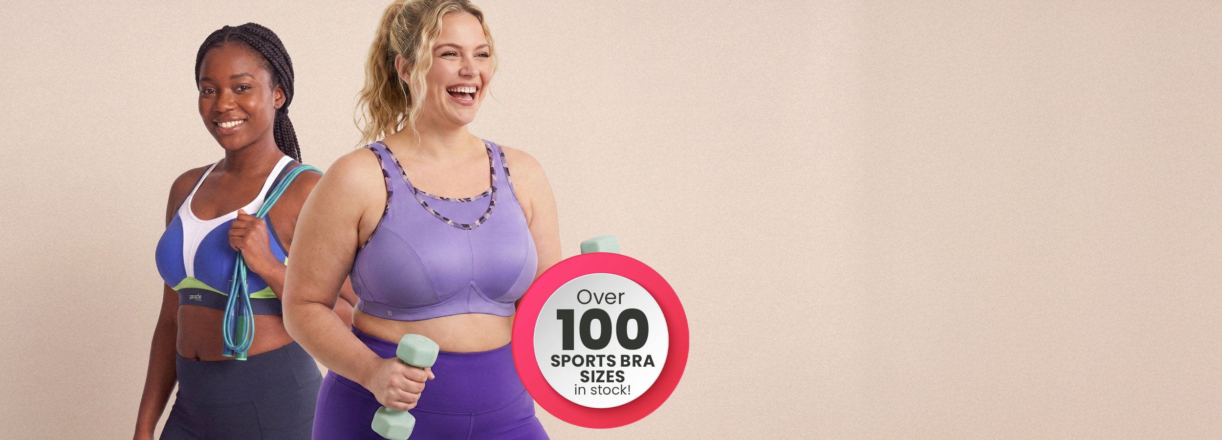 Two women in athletic wear pose against a plain beige background, with a circular badge on the right reading 'Over 100 Sports Bra Sizes'. The woman in front wears a purple sports bra and matching leggings, while the woman behind wears a blue and white sports bra with dark leggings.